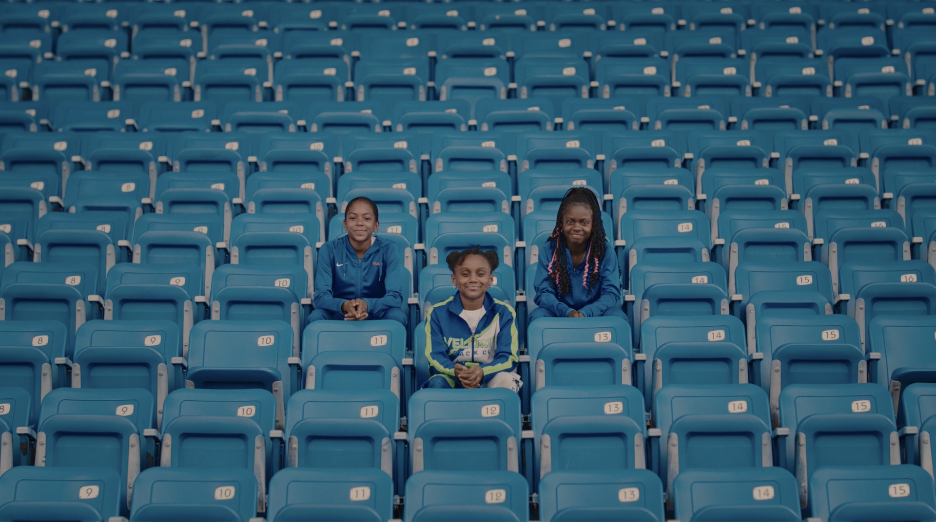 Wide shot of the three young athletes seated together in the empty stands