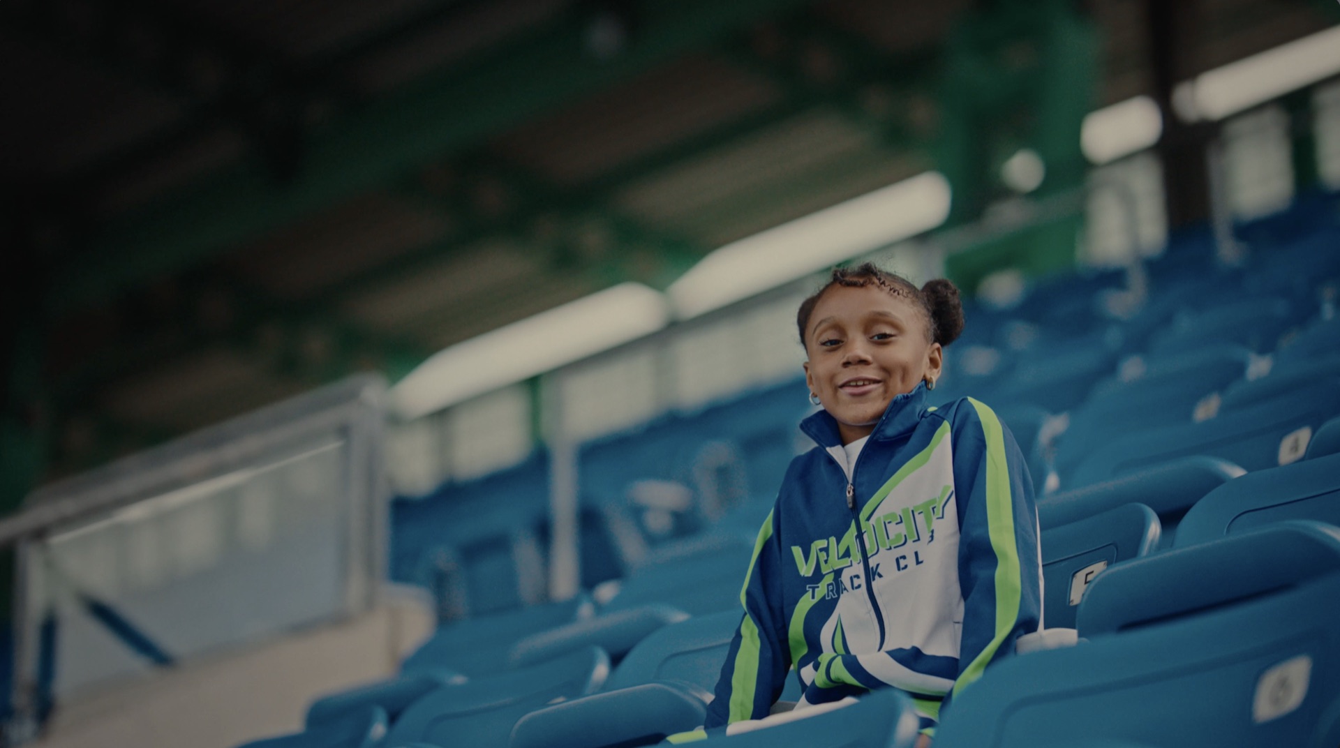 Young athlete in a Velocity Track Club jacket smiling from the stands