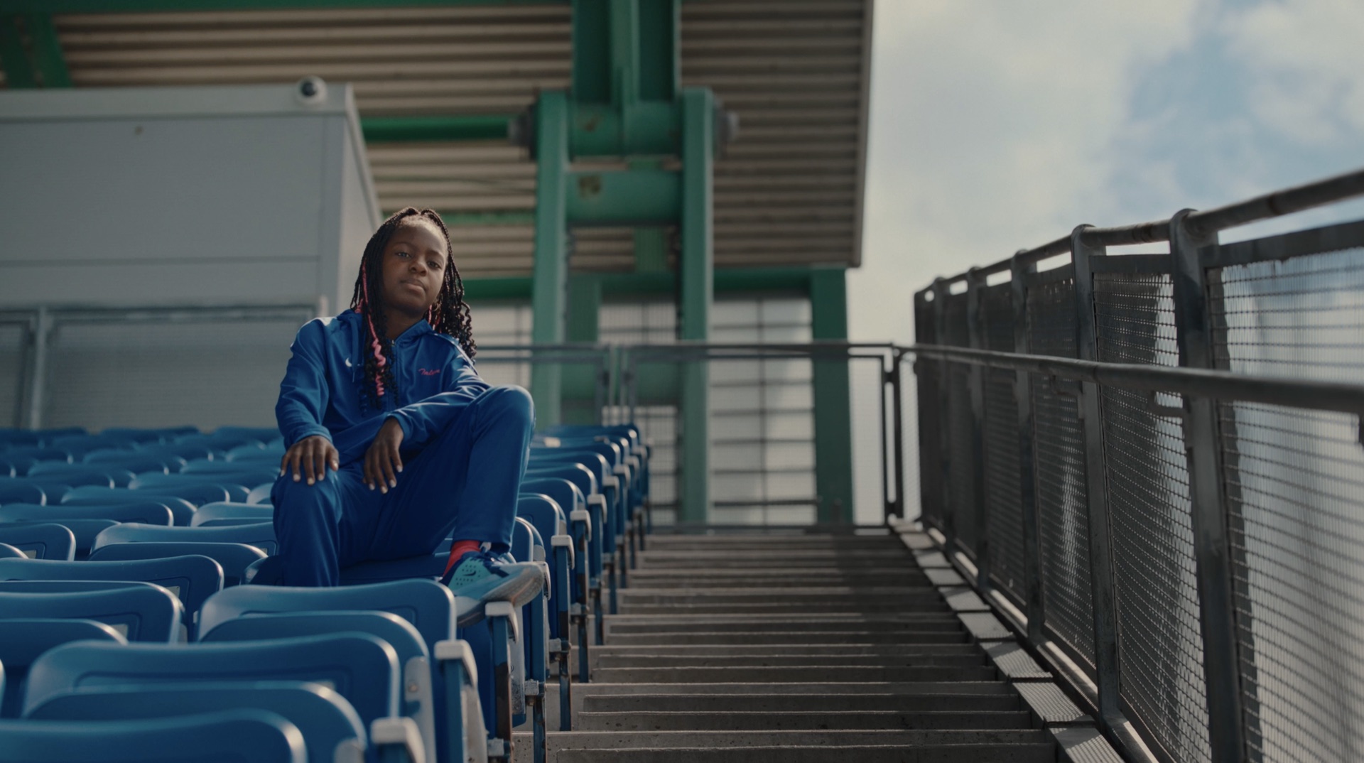 Young athlete seated on stadium stairs beneath the grandstand roof