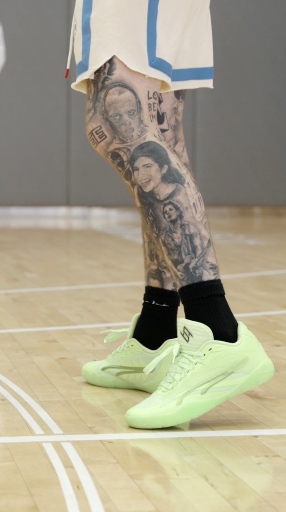 Close-up of tattooed legs and green Puma sneakers on court