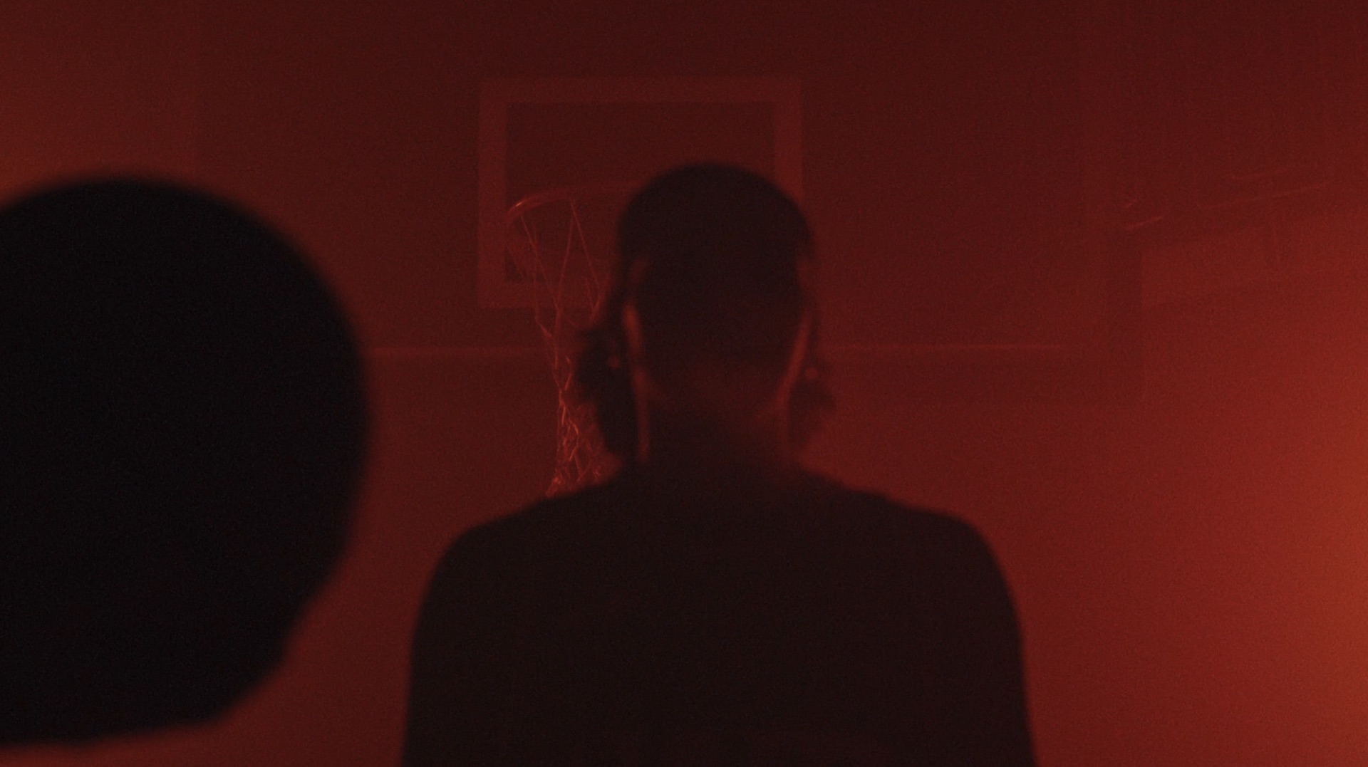 Silhouette of a player facing a basketball hoop, deep red lighting