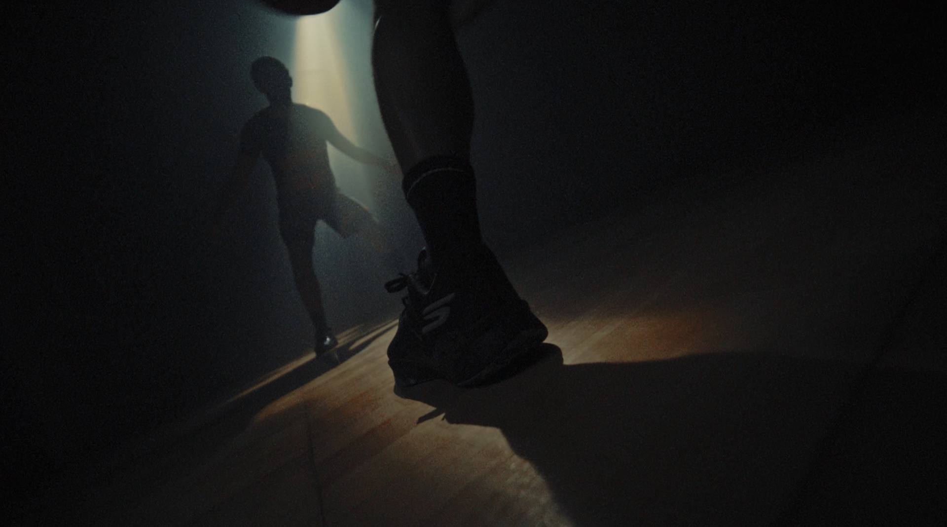 Close-up of a sneaker mid-stride with a blurred runner silhouette in a dim hallway