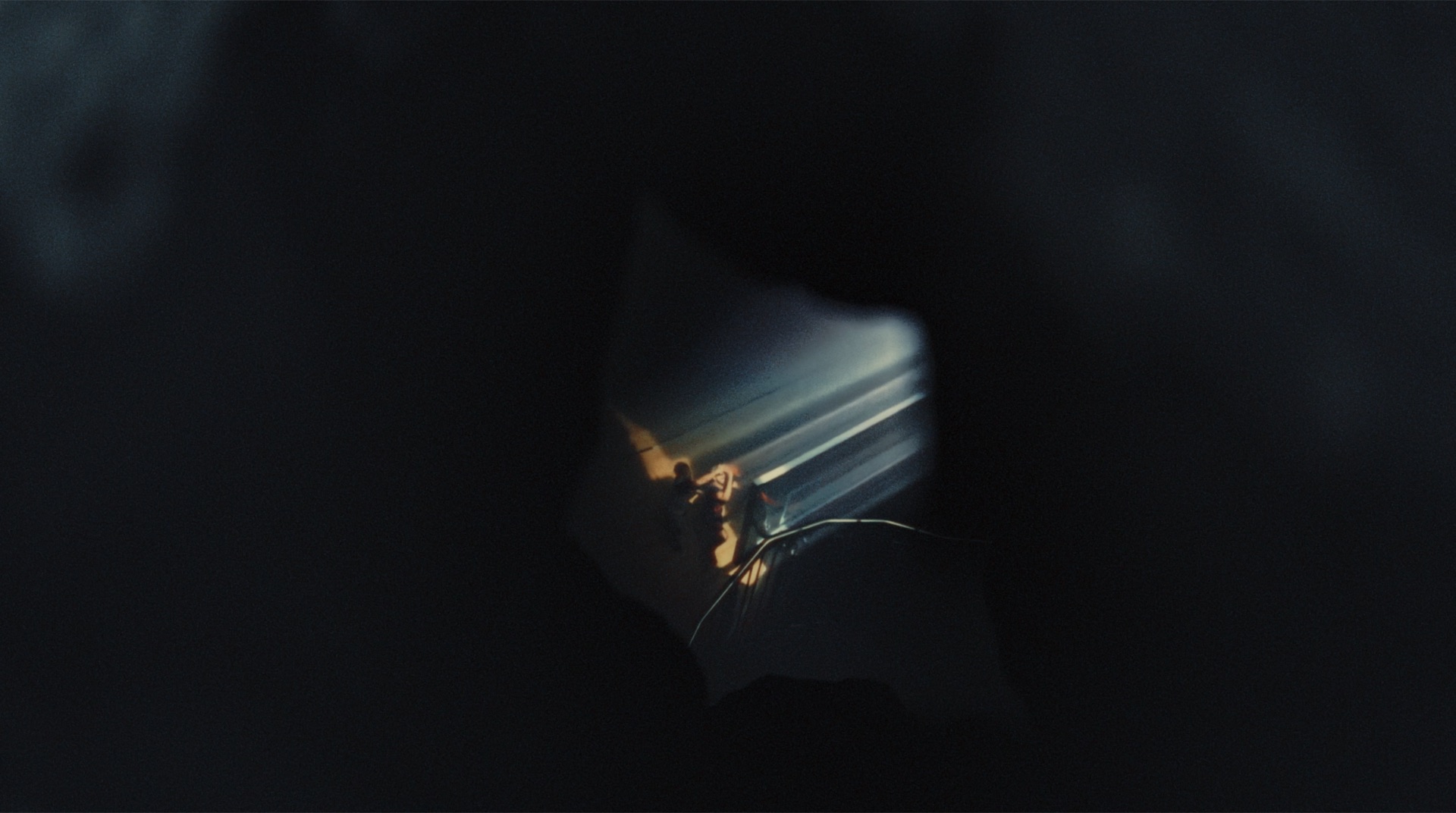 Abstract reflection glimpsed through a dark gap, faint figures visible inside a lit triangular opening