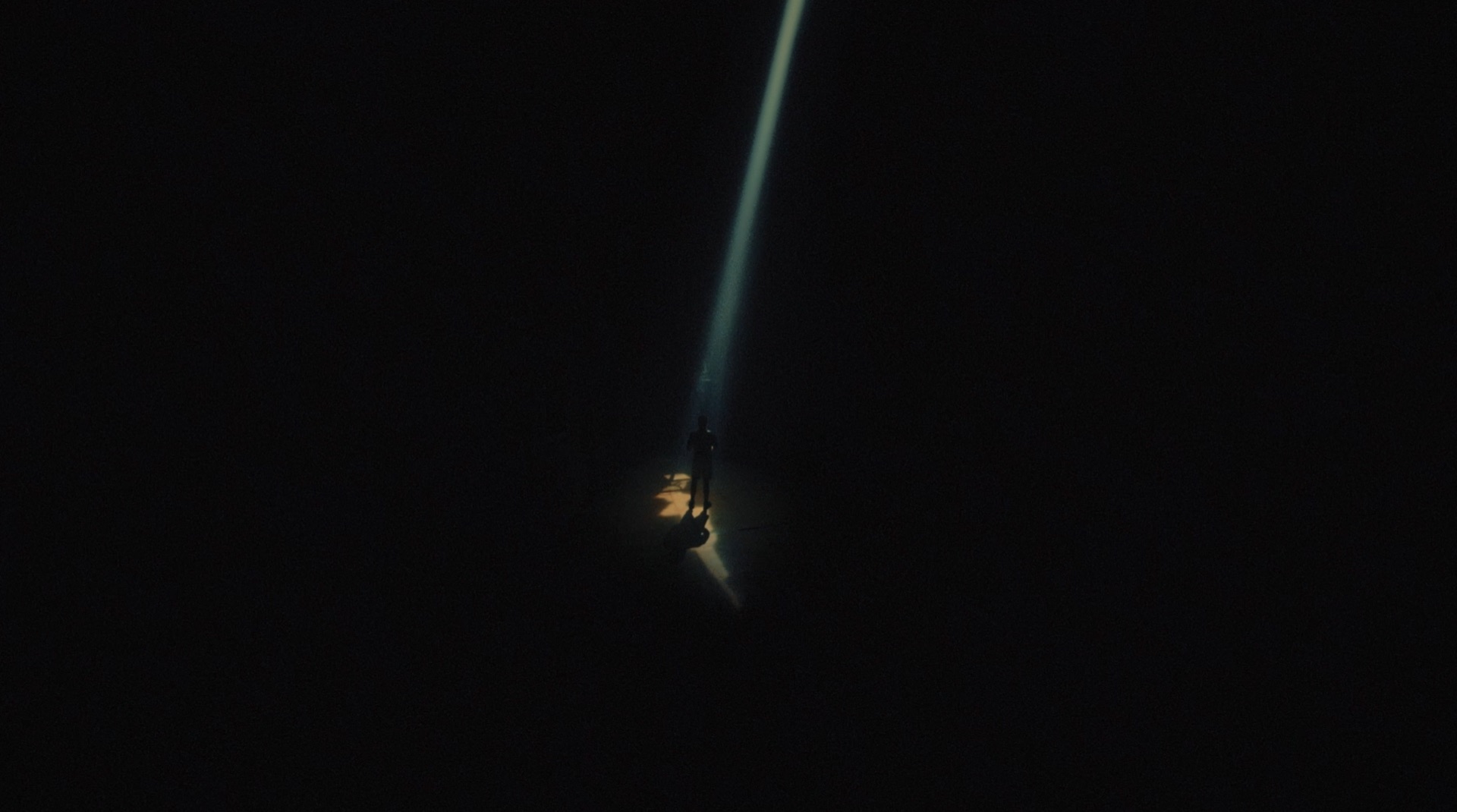 Distant figure standing in a narrow beam of light in a dark space