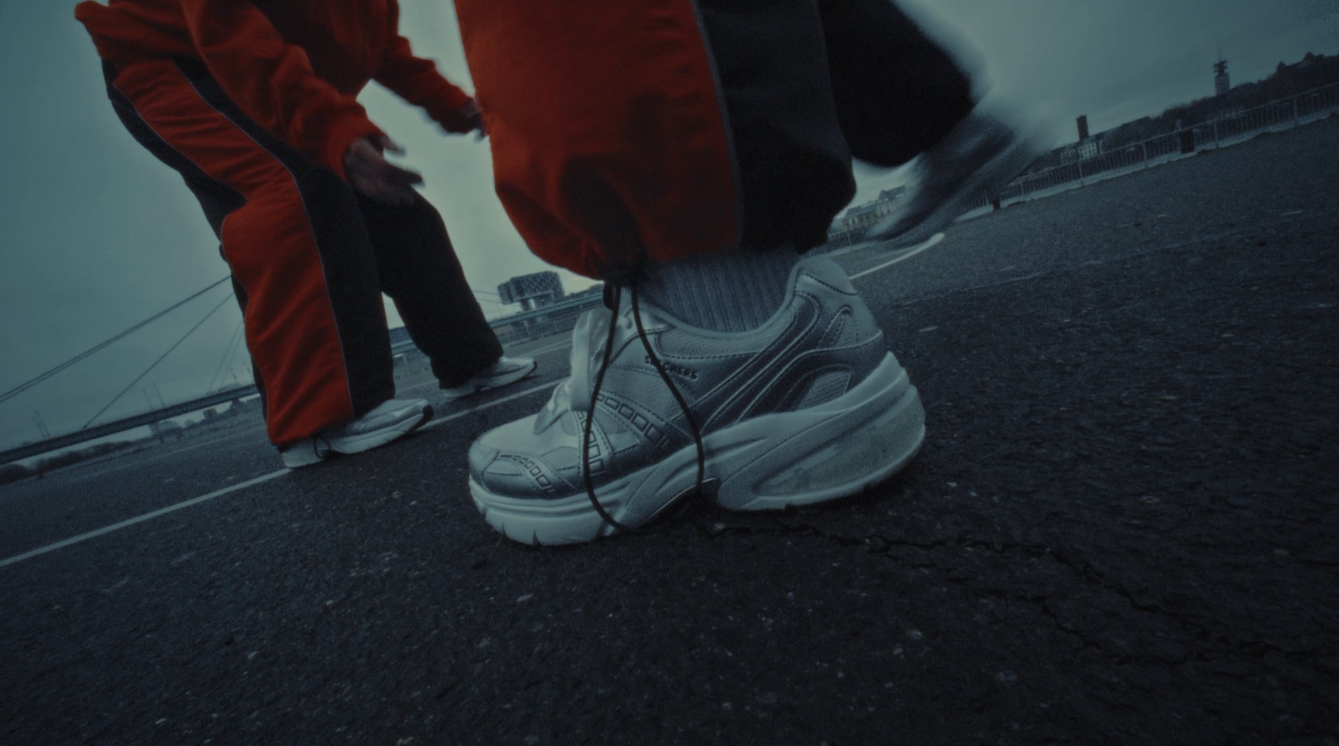 Close-up of white sneakers and orange tracksuit pants on a bridge walkway