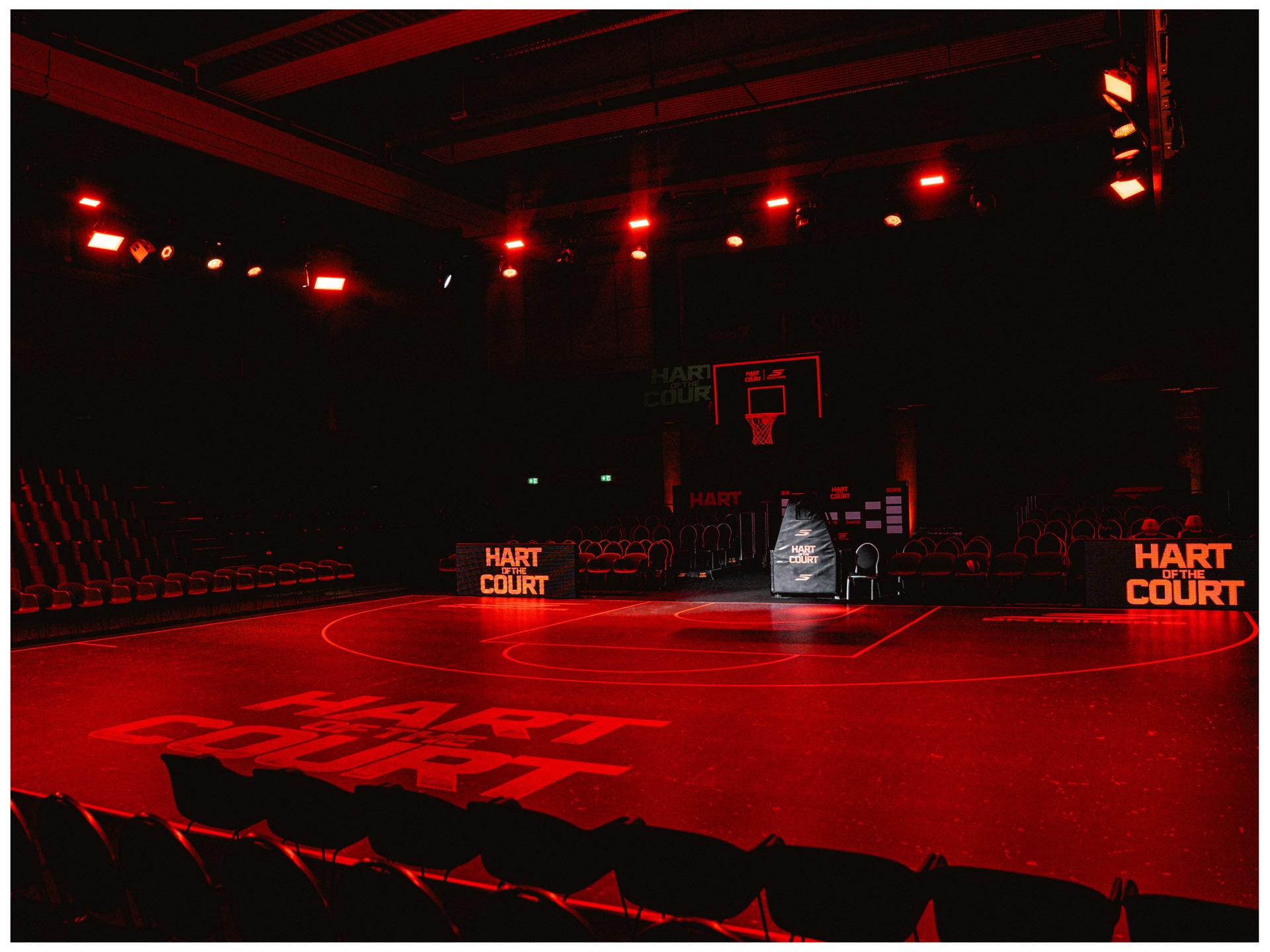 Empty arena bathed in red light, HART OF THE COURT lettering painted on the court