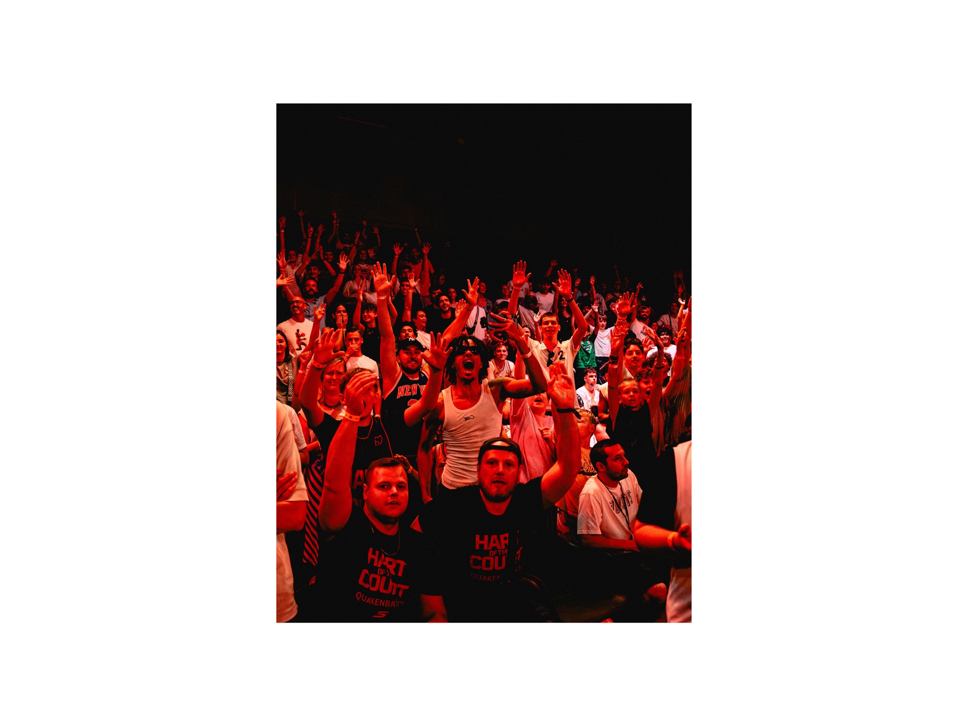 Large crowd with hands raised under red stage lighting, fans wearing HART OF THE COURT shirts up front